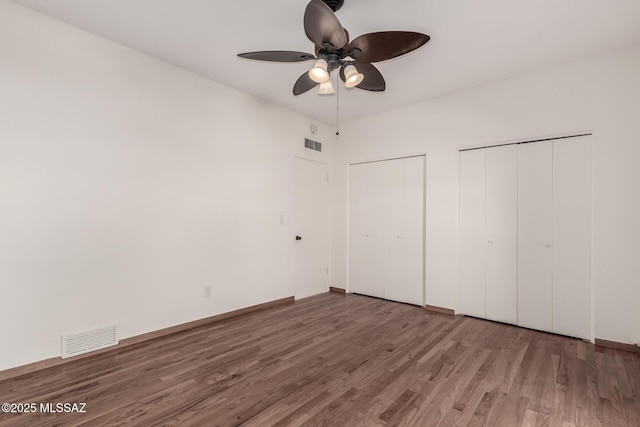 unfurnished bedroom featuring a ceiling fan, wood finished floors, visible vents, and multiple closets