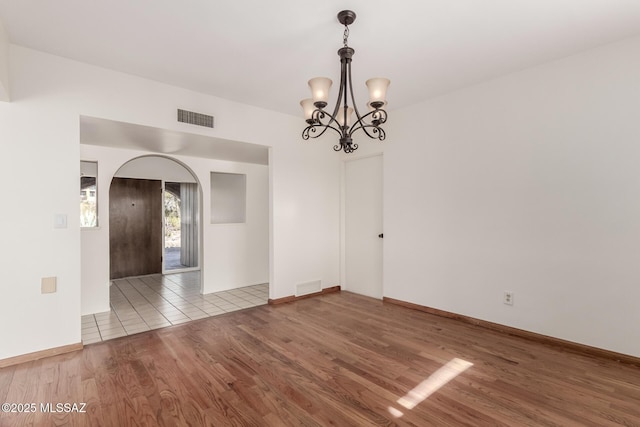 empty room featuring light wood finished floors, visible vents, and arched walkways