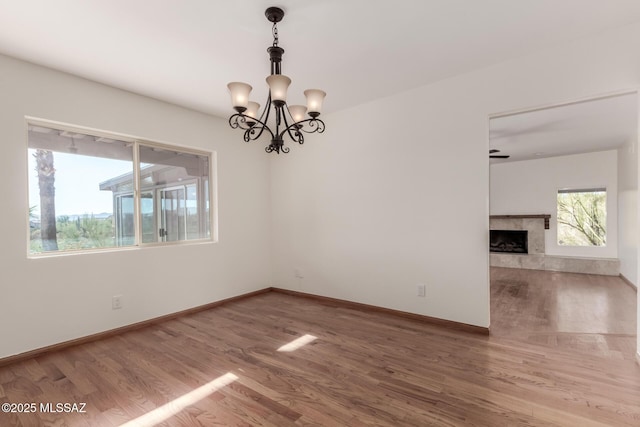 empty room featuring baseboards, a notable chandelier, a premium fireplace, and wood finished floors