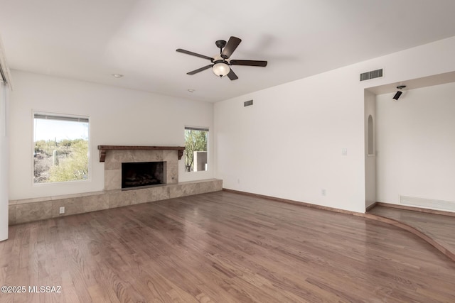 unfurnished living room featuring ceiling fan, a premium fireplace, wood finished floors, and visible vents