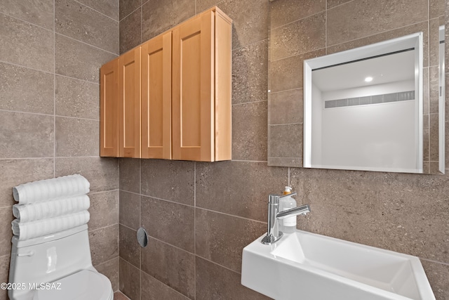 bathroom with toilet, tile walls, and a sink