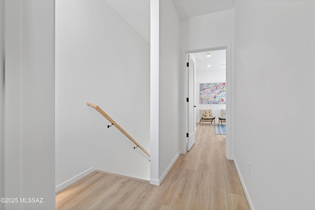 hall featuring light wood-type flooring, baseboards, and an upstairs landing