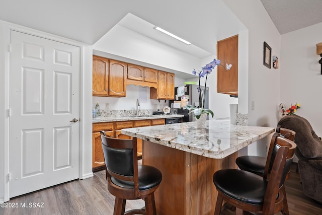 kitchen featuring a breakfast bar, stainless steel fridge, brown cabinetry, and a sink