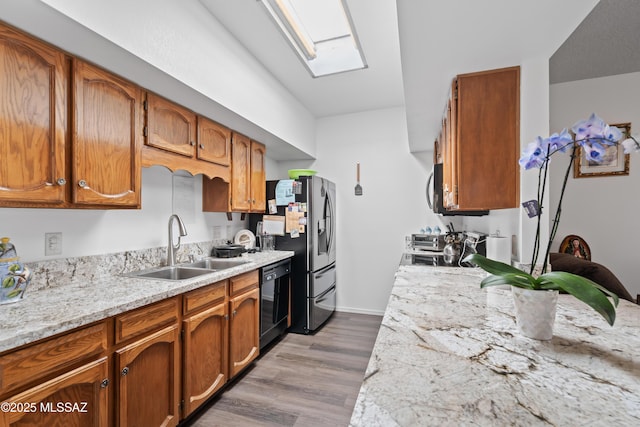 kitchen with a skylight, black dishwasher, brown cabinets, a sink, and wood finished floors