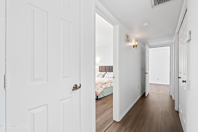 hall with baseboards, visible vents, and dark wood-type flooring