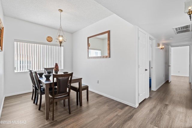 dining area with visible vents, a textured ceiling, baseboards, and wood finished floors