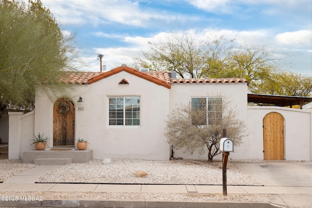 mediterranean / spanish house featuring stucco siding, fence, and a tiled roof