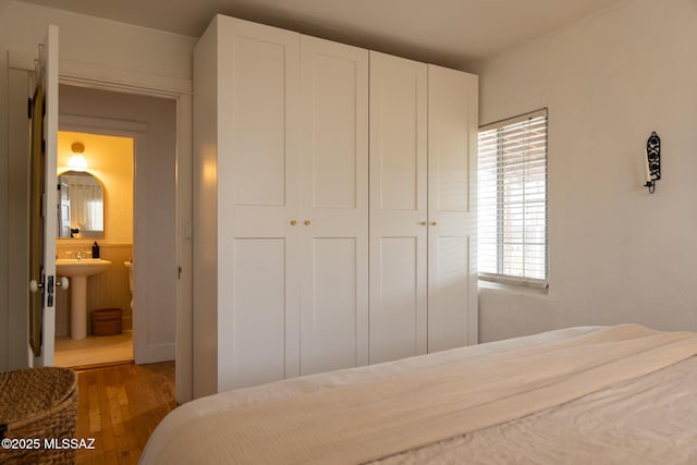 bedroom with a closet, a sink, ensuite bathroom, and wood finished floors