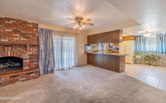 kitchen featuring a fireplace, brown cabinetry, freestanding refrigerator, light carpet, and a peninsula