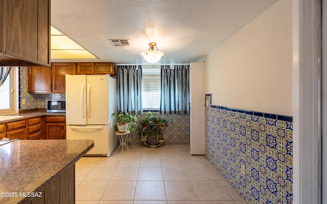 kitchen with light tile patterned floors, dark countertops, stainless steel microwave, freestanding refrigerator, and a textured ceiling