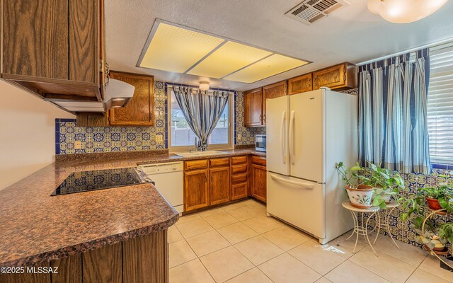 kitchen featuring white appliances, a sink, visible vents, brown cabinets, and dark countertops