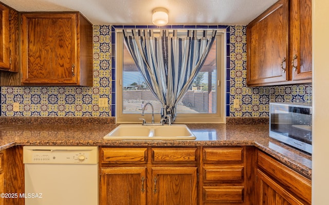kitchen featuring white dishwasher, a sink, backsplash, stainless steel microwave, and dark countertops