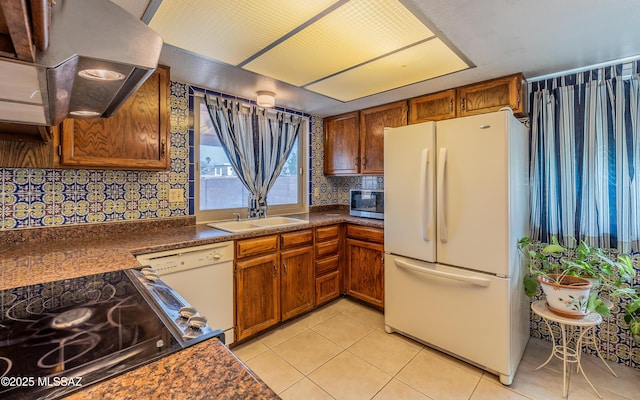 kitchen featuring light tile patterned flooring, white appliances, a sink, exhaust hood, and dark countertops