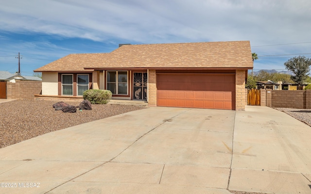 ranch-style house with concrete driveway, roof with shingles, fence, and an attached garage