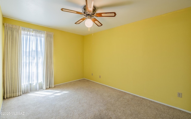 carpeted spare room featuring a ceiling fan and baseboards