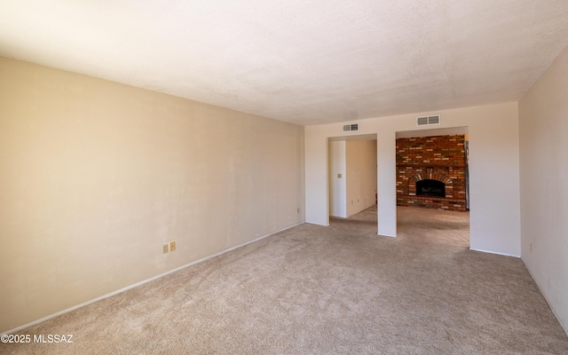 empty room featuring carpet, visible vents, a fireplace, and a textured ceiling