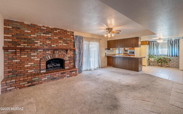 unfurnished living room featuring light carpet, a brick fireplace, ceiling fan, and a textured ceiling
