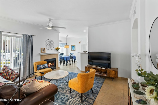 living area with ornamental molding, a ceiling fan, a tile fireplace, and light tile patterned floors