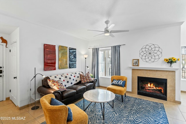 tiled living room featuring ceiling fan, a fireplace, baseboards, and crown molding