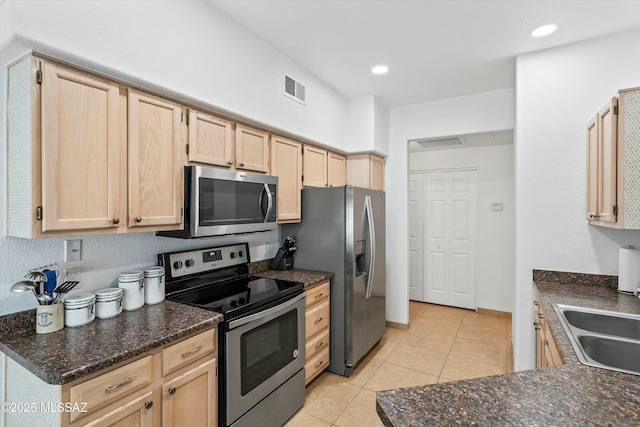 kitchen featuring light tile patterned floors, stainless steel appliances, a sink, visible vents, and light brown cabinetry