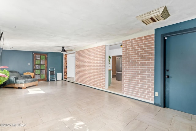 spare room with visible vents, ceiling fan, and brick wall