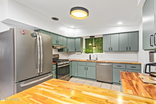 kitchen with light tile patterned floors, green cabinets, appliances with stainless steel finishes, butcher block countertops, and under cabinet range hood