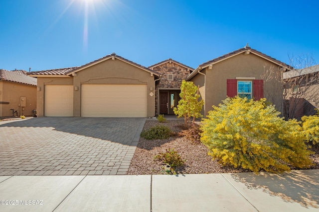 view of front facade featuring decorative driveway, a tile roof, stucco siding, a garage, and stone siding