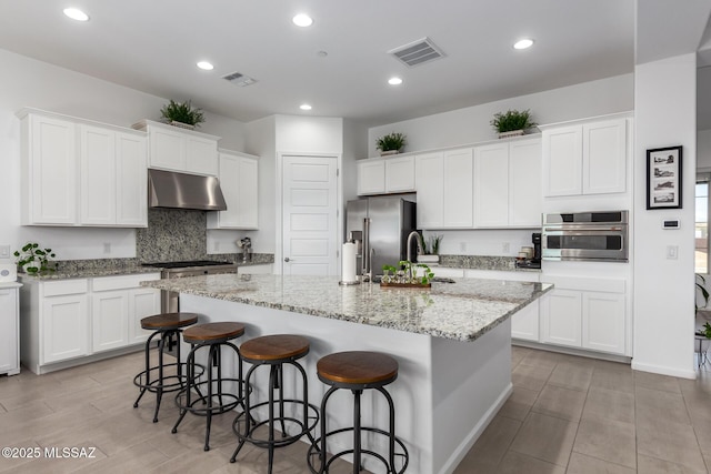 kitchen with appliances with stainless steel finishes, visible vents, a center island with sink, and under cabinet range hood