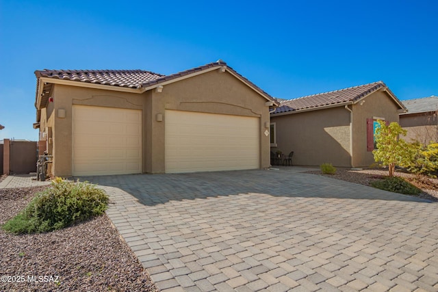 view of front facade with a garage, a tile roof, decorative driveway, and stucco siding