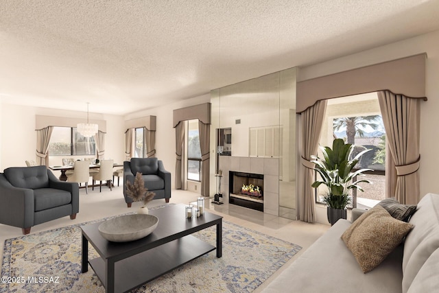 living room featuring light carpet, a notable chandelier, a textured ceiling, and a tiled fireplace