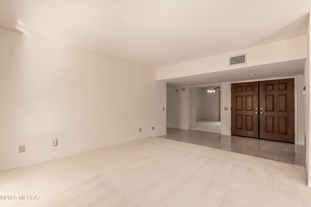 spare room with light tile patterned floors, a textured ceiling, light carpet, visible vents, and a ceiling fan