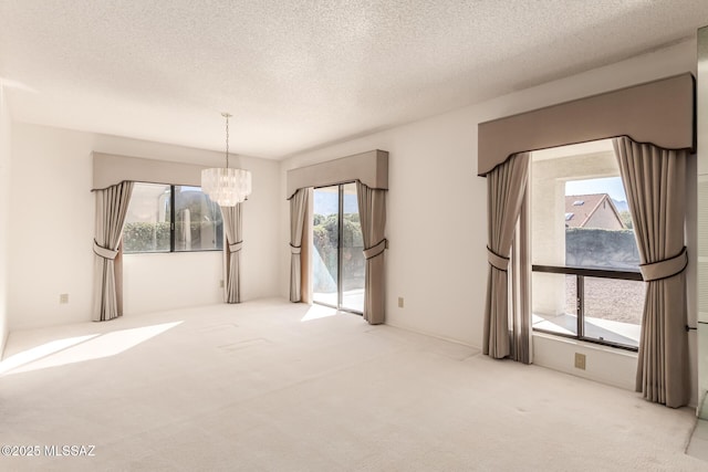 carpeted empty room with a textured ceiling and a notable chandelier