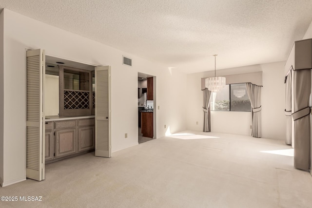 interior space with light carpet, a textured ceiling, visible vents, and a notable chandelier