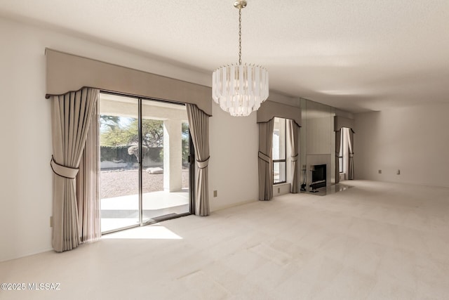 unfurnished living room featuring carpet flooring, a fireplace, a textured ceiling, and an inviting chandelier