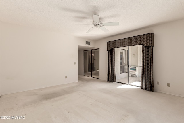 unfurnished room with light colored carpet, visible vents, ceiling fan, and a textured ceiling