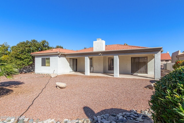 back of property featuring a tiled roof, a chimney, a patio area, and stucco siding