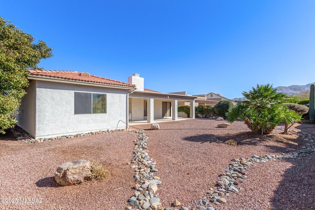 back of property featuring a chimney, a tiled roof, and stucco siding