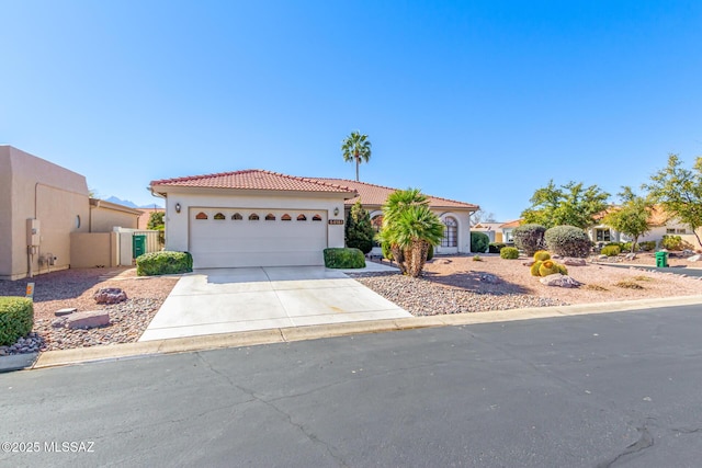 mediterranean / spanish home with an attached garage, fence, concrete driveway, a tiled roof, and stucco siding