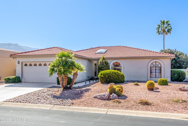 mediterranean / spanish house with a garage, a tiled roof, concrete driveway, and stucco siding