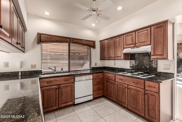 kitchen featuring tasteful backsplash, a sink, dark stone counters, white appliances, and under cabinet range hood