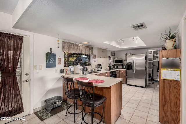 kitchen with light countertops, appliances with stainless steel finishes, a sink, a peninsula, and a kitchen breakfast bar