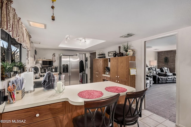 kitchen featuring a tray ceiling, brown cabinets, light countertops, visible vents, and appliances with stainless steel finishes