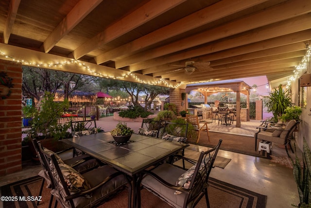 patio terrace at dusk featuring ceiling fan, outdoor dining area, and exterior bar