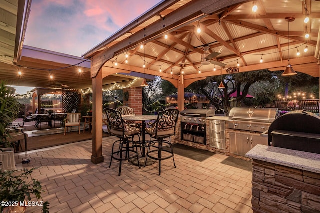 patio terrace at dusk featuring an outdoor bar, area for grilling, and a gazebo