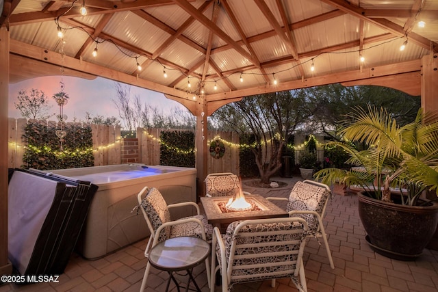 patio terrace at dusk with fence, a fire pit, and a gazebo