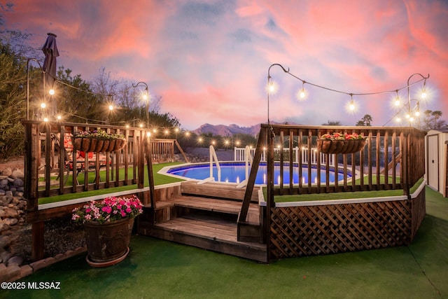 pool with a storage shed, a deck with mountain view, and a lawn