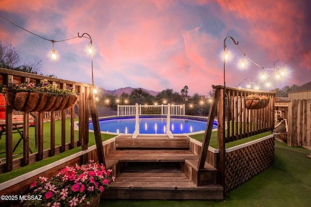 pool at dusk featuring a yard, an outdoor pool, and fence