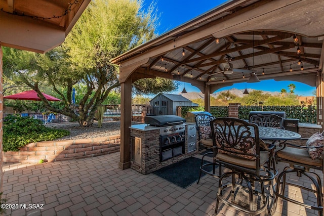 view of patio / terrace with an outdoor kitchen, a fenced backyard, ceiling fan, grilling area, and a gazebo