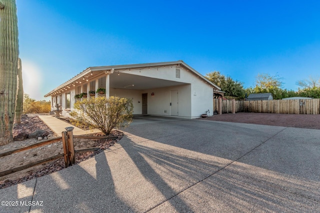 view of front of house featuring an attached carport, stucco siding, driveway, and fence