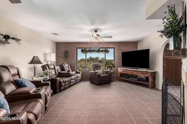 living area featuring light tile patterned floors, visible vents, arched walkways, and a ceiling fan